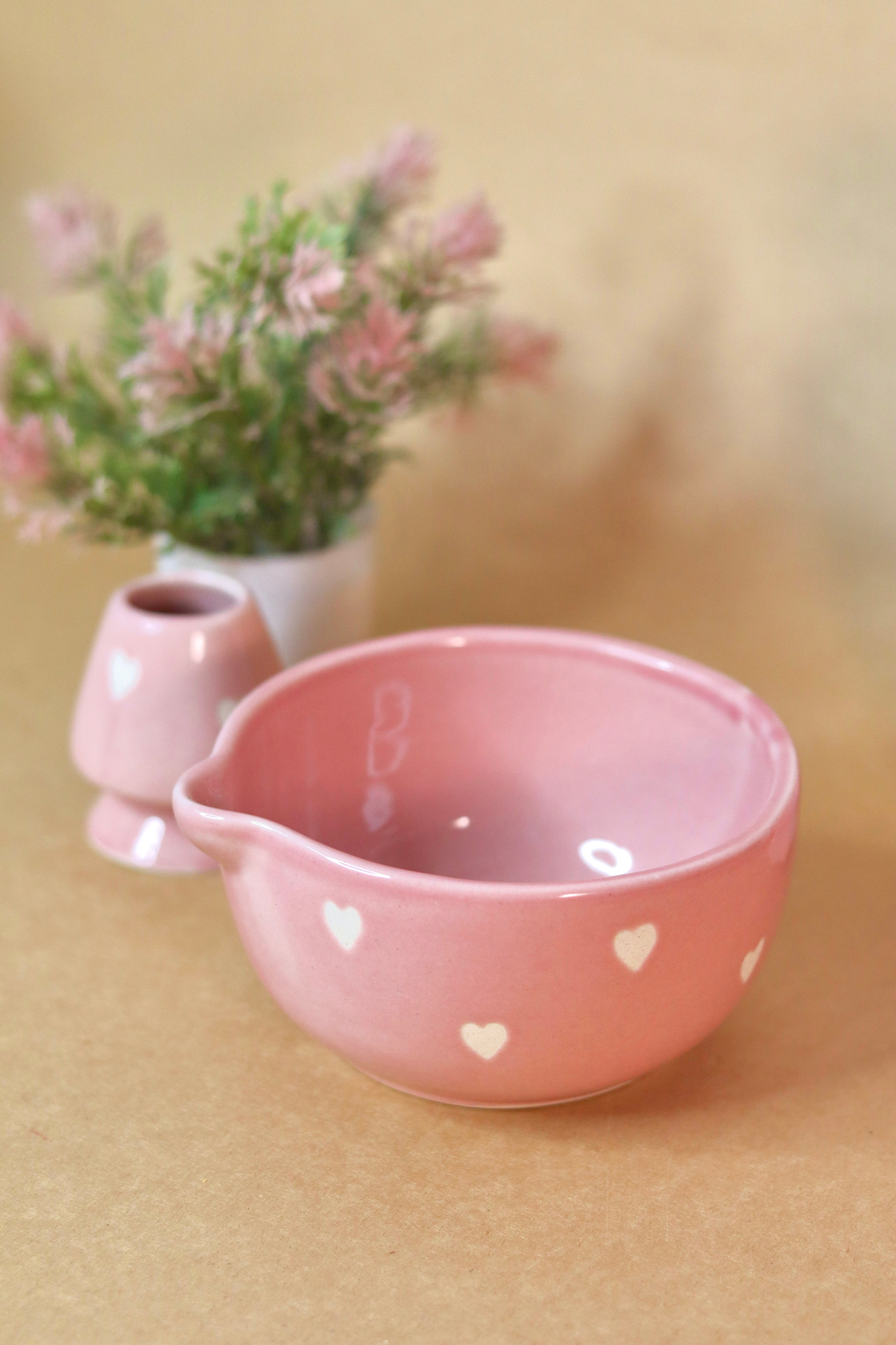Pink ceramic bowl with heart patterns on a beige surface with a blurred background