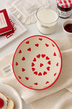 A cream-colored ceramic bowl with a red rim and a pattern of small red hearts,