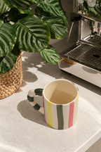 A ceramic coffee mug with vertical stripes in green, white, yellow, and pink