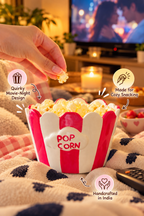 A hand reaches into a red and white striped popcorn bowl filled with popcorn