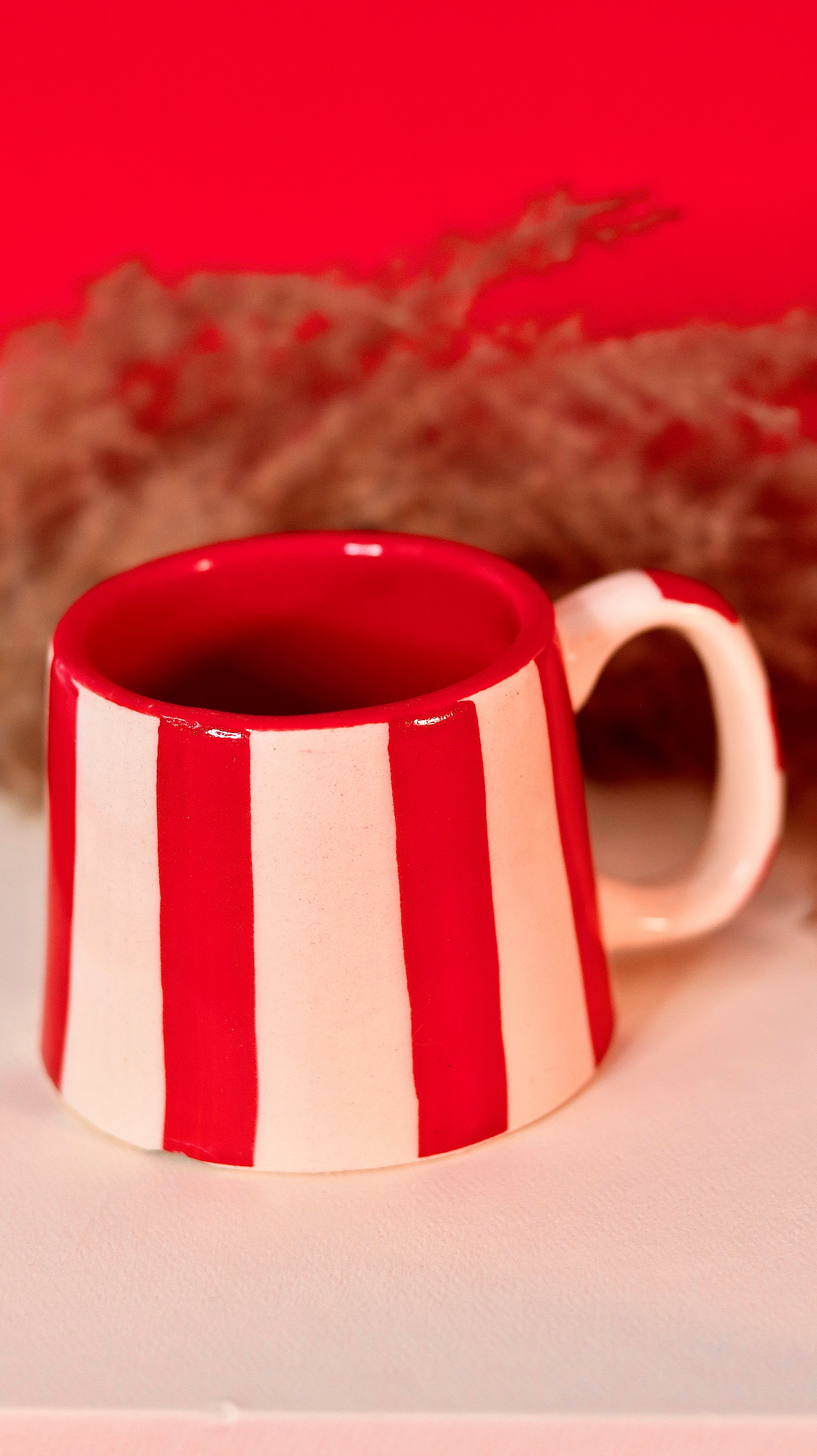 Red and white striped mug on a light surface with a blurred red background